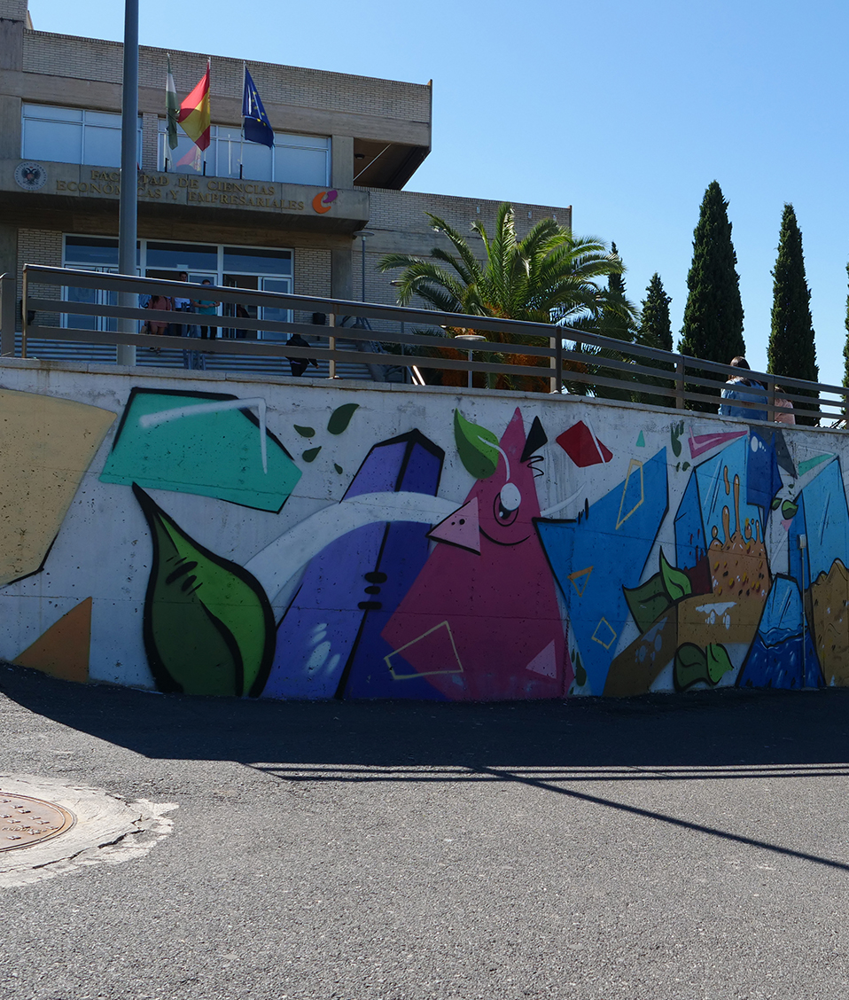 Pared con un grafiti en la Facultad de Ciencias Económicas y Empresariales de Granada. Al fondo se ve la fachada de la Facultad