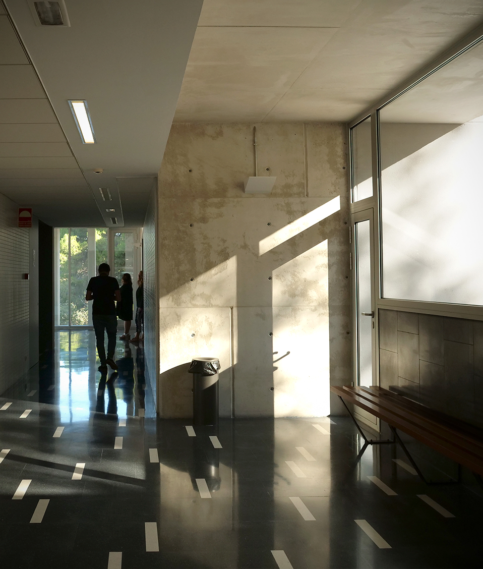 Sala de la Facultad de Ciencias Económicas y Empresariales de Granada con estudiantes al final de un pasillo. A la derecha hay un banco